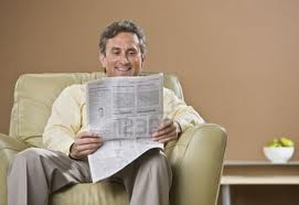 He is sitting down reading a newspaper